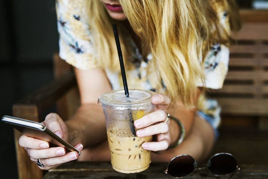 Girl using mobile phone while sipping iced coffee