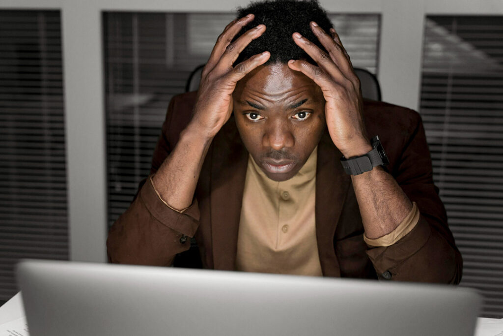 Man holding his head in his hands, looking at his laptop screen after data breaches.